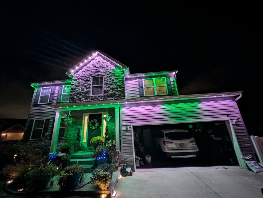 Stone colonial home with green and purple roofline lighting