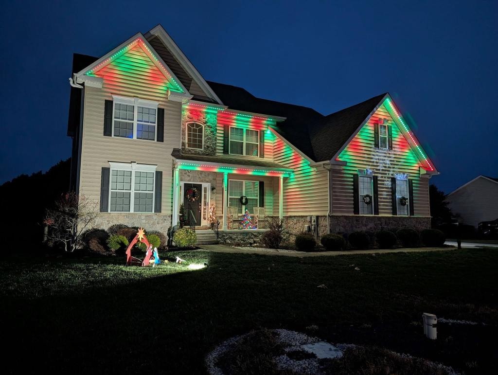 Large colonial home with red and green Christmas roofline lighting